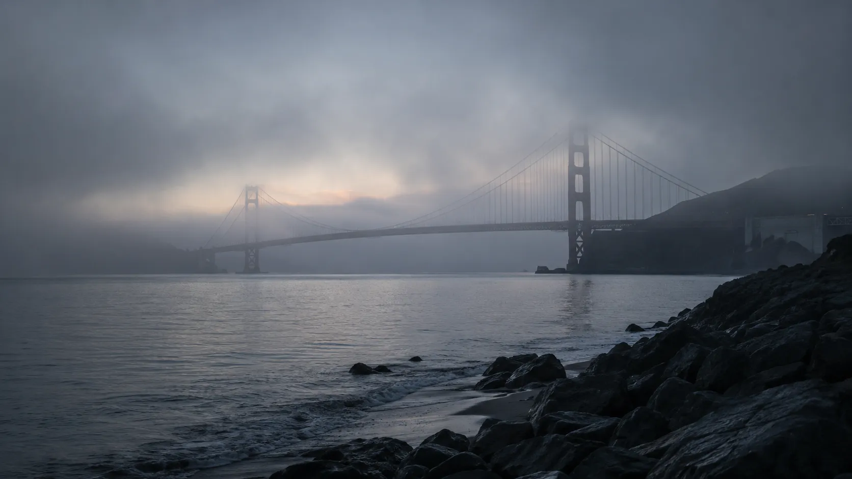 A fog-shrouded bay bridge at dawn seen from a rocky shore, used as symbolic cover art for the Laci Peterson case.